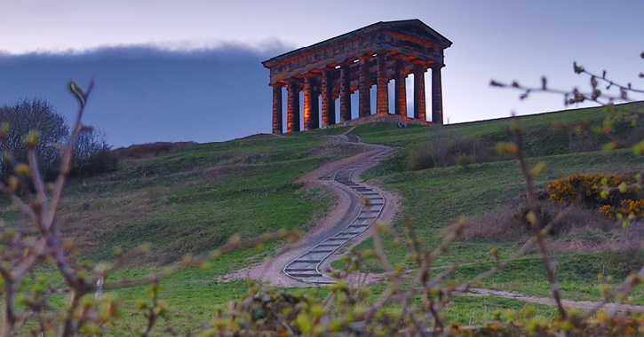 View of Penshaw Monument on a cloudy day with the monument covered in red lighting.  